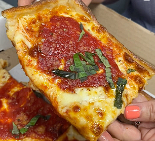 someone holding a slice of pizza with a lot of sauce and basil