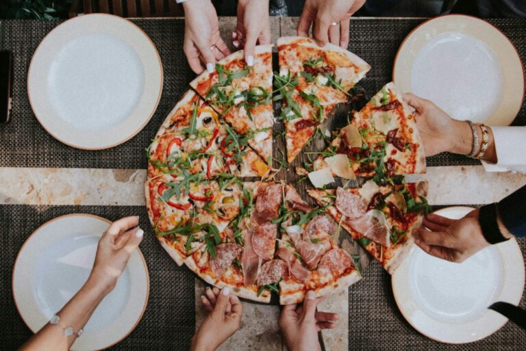 people are holding their hands over a pizza on a table