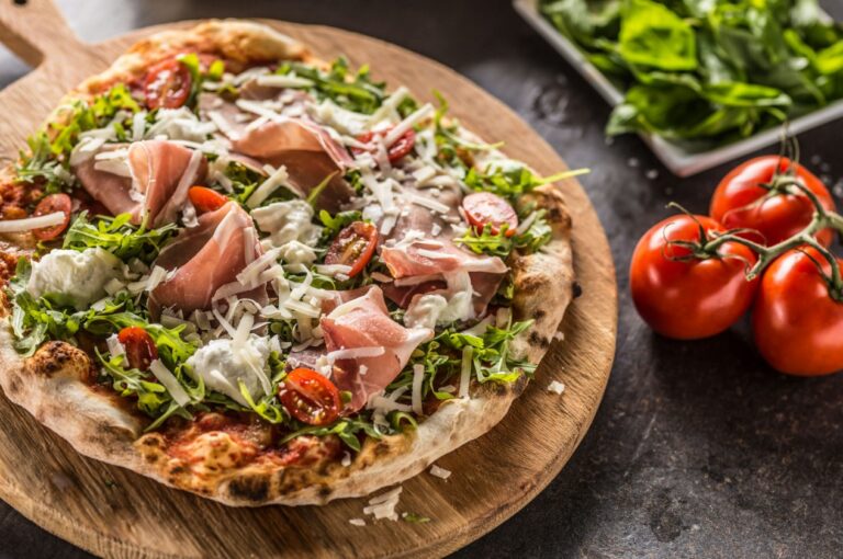 a close up of a pizza with meat and vegetables on a wooden board